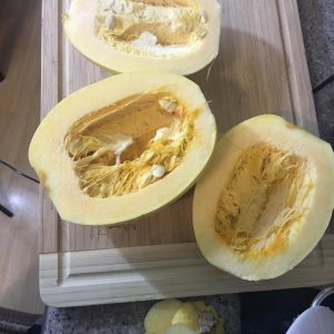 Three spagehtti squash cut in half on a cutting board.