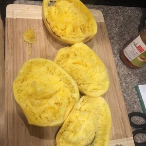 Spaghetti squash strands in cooked squash halves on a cutting board.